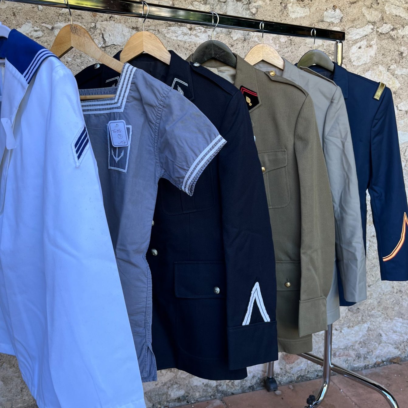 uniformes militaire armée française de différentes couleurs et de régiments  accrochés à un portant.