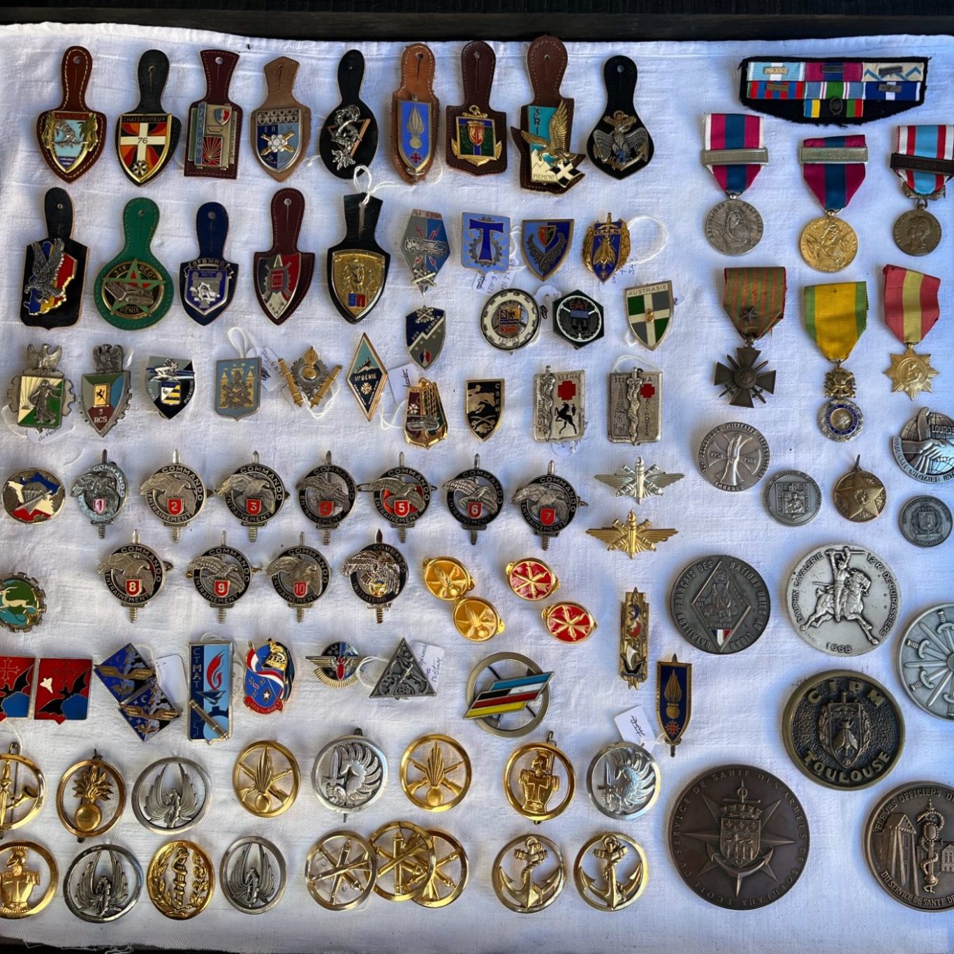 Collection de médailles militaire, insignes armée de terre variés disposés sur un tissu blanc dans une vitrine